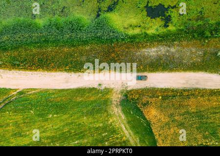 Vista aerea del SUV auto parcheggiato sulla strada di campagna tra il campo rurale e il paesaggio paludoso di Marsh Bog. Giorno d'estate Foto Stock