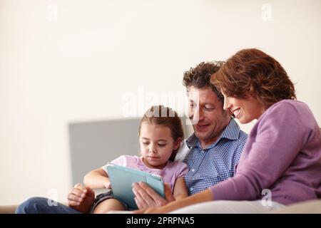 Trovare cose divertenti da fare online. Una bambina che utilizza un tablet digitale bianco seduto con i genitori. Foto Stock