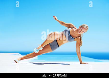 I migliori allenamenti usano il corpo come strumento. Una giovane donna che lavora su un patio sotto un cielo blu. Foto Stock