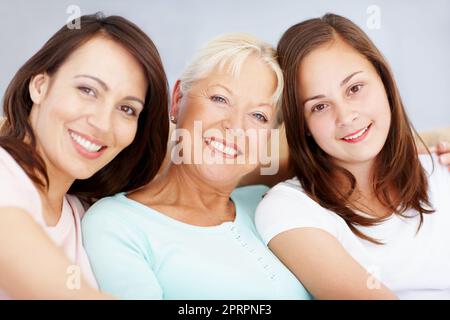 Bel ritratto delle ragazze di famiglia. Tre generazioni di ragazze che si siedono insieme sul divano del salotto sorridendo insieme. Foto Stock