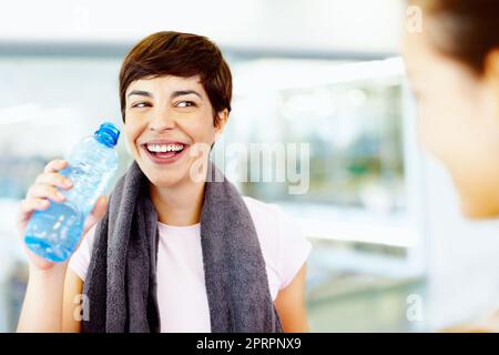 Femmine rinfrescanti dopo l'allenamento in palestra. Donna beve acqua mentre chiacchiera con gli amici al centro fitness. Foto Stock