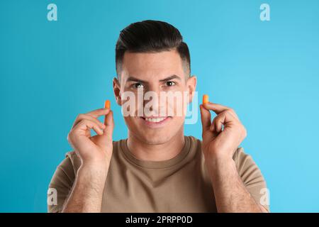 Uomo con tappi auricolari in schiuma su sfondo azzurro Foto Stock