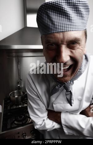 Chef maturo divertente in piedi di fronte alla stufa a gas e cappa di ventilazione. Primo piano ritratto di un divertente chef maturo in piedi di fronte alla stufa a gas e cappa di ventilazione. Foto Stock