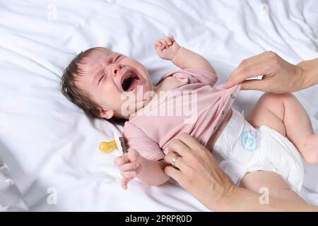 Madre che mette i vestiti sulla figlia piangente sul letto, primo piano Foto Stock