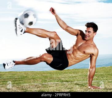 Giovane giocatore di calcio che calcia il calcio in azione. Ritratto di un giovane giocatore di calcio che calcia il calcio in azione contro il cielo. Foto Stock