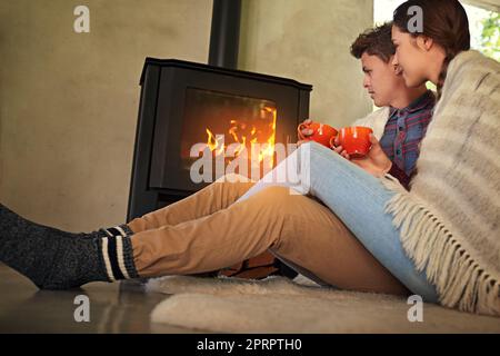 Questa stagione, una giovane coppia beve cioccolata calda accanto al caminetto. Foto Stock