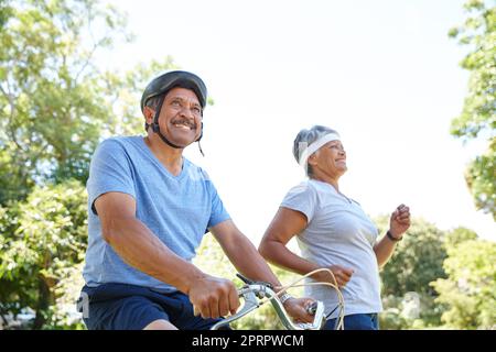 In forma per la vita. Una coppia anziana felice che va per un giro in bicicletta e una corsa insieme all'aperto. Foto Stock