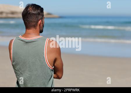 Trovare pace e tranquillità in mare. Ripresa da dietro di un giovane uomo che guarda l'oceano. Foto Stock