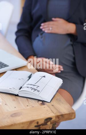 Non molto tempo... Un notebook con dettagli sul congedo di maternità sdraiato su una scrivania incinta di womanamp039s mentre tiene lo stomaco. Foto Stock