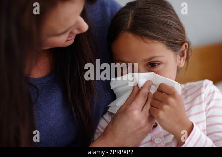 Achoo. Una madre che aiuta la figlia ammalata a soffiare il naso. Foto Stock