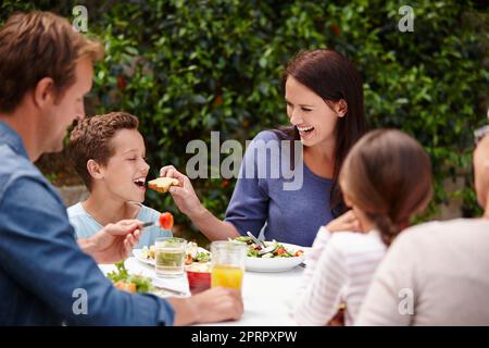 Condividere è prendersi cura, una famiglia felice multi-generazionale che ha un pasto insieme all'esterno. Foto Stock