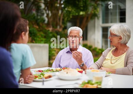 Trasmettere la saggezza. Una famiglia multi-generazionale felice che ha un pasto insieme fuori. Foto Stock