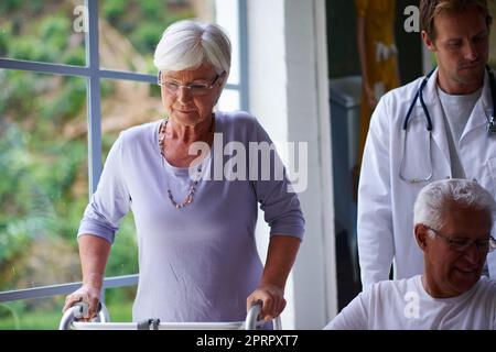 Fare progressi. Due persone anziane che sono aiutate da personale infermieristico. Foto Stock