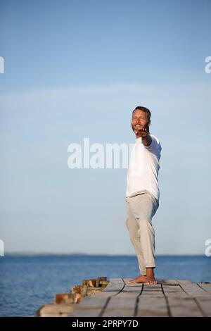 Un bell'uomo maturo che fa yoga su un molo sull'oceano. Foto Stock