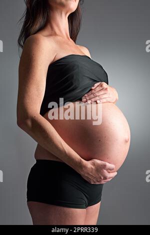 Aspettandosi il suo arrivo presto. Una donna incinta che tiene la pancia. Foto Stock