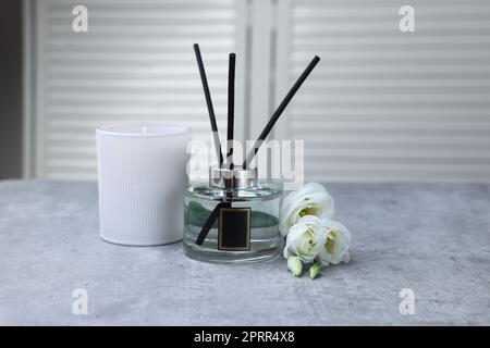 Diffusore a canna, candela profumata e fiori di eustoma su tavolo in marmo grigio Foto Stock