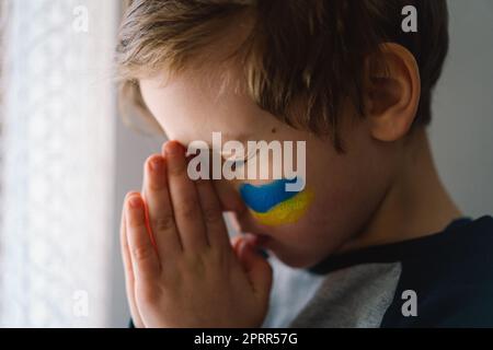 Il ragazzo ucraino chiuse gli occhi e pregava per fermare la guerra in Ucraina. Foto Stock