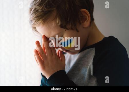 Il ragazzo ucraino chiuse gli occhi e pregava per fermare la guerra in Ucraina. Foto Stock