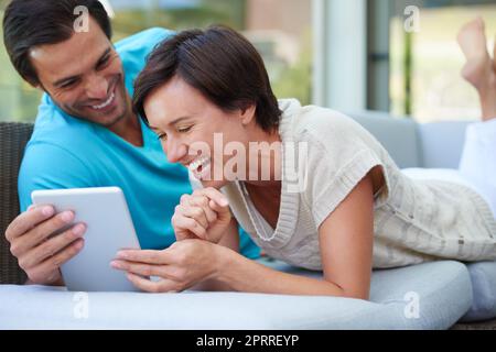 Hanno lo stesso senso dell'umorismo. Una coppia con un tablet che ride di qualcosa di divertente online. Foto Stock