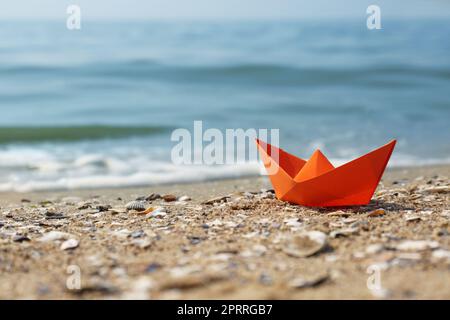 Barca di carta arancione sulla spiaggia sabbiosa vicino al mare, spazio per il testo Foto Stock