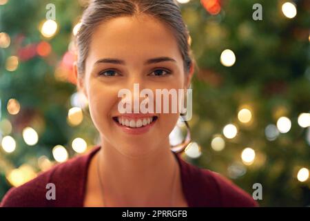 Sorrisi natalizi. Ritratto di una bella giovane donna di fronte ad un albero di natale. Foto Stock