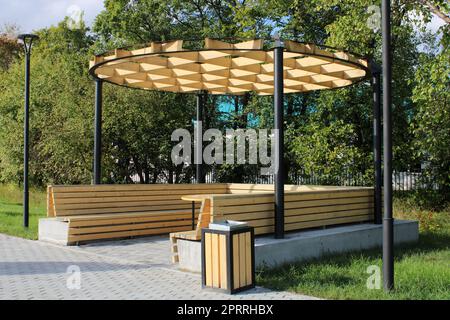 Un gazebo di legno chiaro con una panca, un tavolo e un insolito hutch in un parco cittadino. Architettura urbana Foto Stock