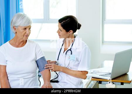 Questo non danneggia affatto. Un medico giovane e bello che esamina la pressione sanguigna dei pazienti anziani. Foto Stock