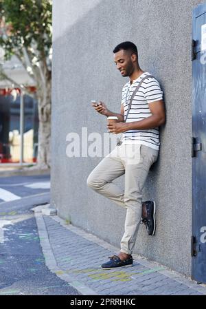 HES costantemente connesso grazie alla tecnologia degli smartphone. Un bell'uomo d'affari afroamericano appoggiato contro un muro della città mentre usa il suo cellulare. Foto Stock