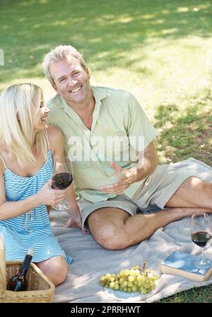 Godendo la raccolta della natura. Un marito e una moglie felici che si godono un bicchiere di vino mentre si ha un pic-nic all'aperto in un parco in una giornata estiva. Foto Stock