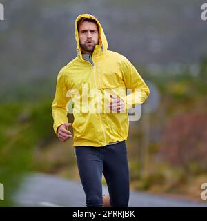 Focus e determinazione per raggiungere i suoi obiettivi. Un bel giovane uomo che corre in tempo piovoso. Foto Stock