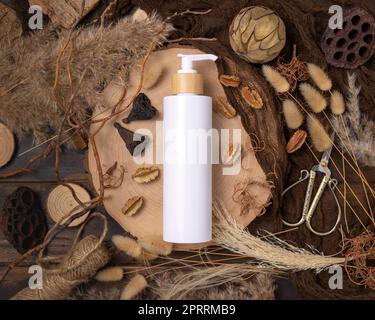 Una bottiglia cosmetica con pompa su legno vicino alle decorazioni boho naturali vista dall'alto. Etichetta Mockup Foto Stock