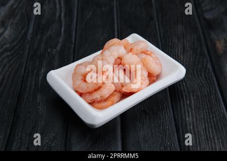 Piccoli gamberetti lessati e sgusciati in piccola piastra su scuro dello sfondo in legno Foto Stock