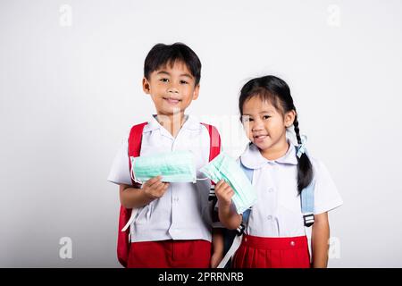 Due studenti asiatici ragazza ragazzo fratello ragazzo fratello indossare studente tailandese uniforme tenere maschera di protezione pronto per andare a scuola Foto Stock