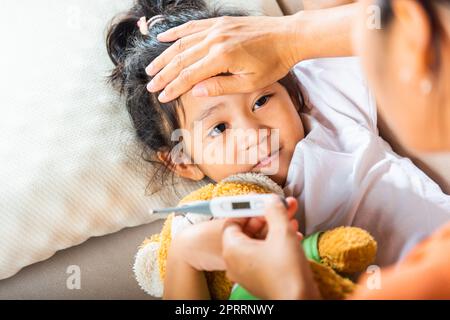 Madre genitore che controlla la temperatura di sua figlia malata con termometro digitale in bocca Foto Stock