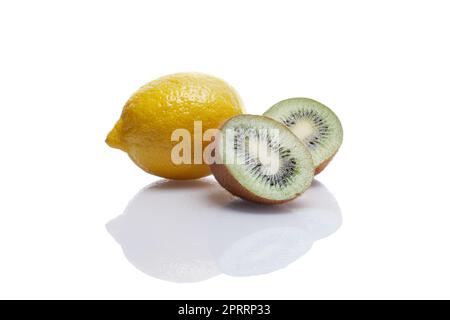 Un limone intero e due pezzi di kiwi con riflessione su tavola di vetro bianco Foto Stock