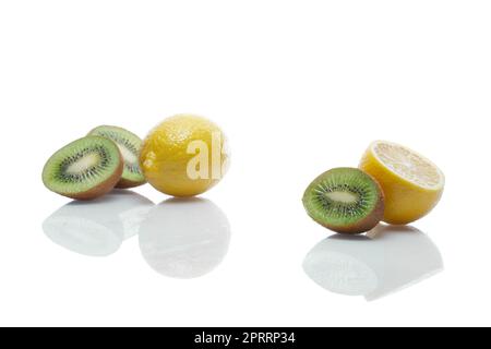 Limoni e kiwi con riflessi su tavola di vetro bianco Foto Stock