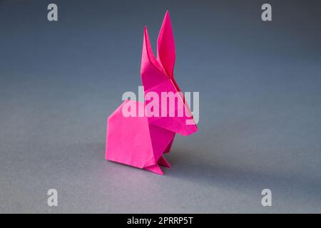 Origami di coniglio di carta rosa isolato su uno sfondo grigio Foto Stock