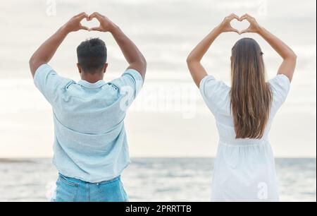 Coppia di mani, cuore alla schiena segno d'amore e passione, affetto o emoji romantica vicino all'oceano. Romanticismo, uomo e donna, simbolo della mano o forma emotiva. Intimità o adorazione, sostegno o gesto di devozione. Foto Stock