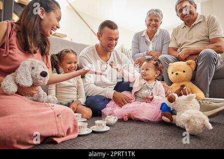 Grande ritratto di famiglia nella stanza dei bambini con giocattoli per il tè e il party per giocare e legare insieme sul pavimento. Nonni, madre e padre felici con un bambino nella loro casa di famiglia divertendosi seduti a terra Foto Stock