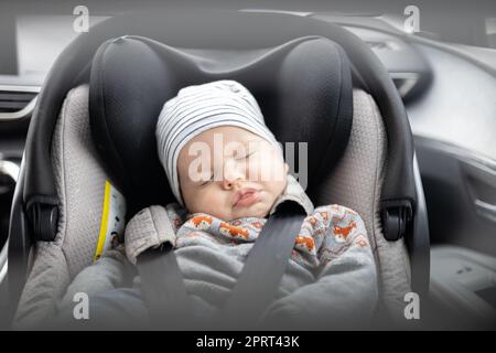 Il bambino piccolo cute che dorme legato nel sedile dell'automobile del bambino nell'abitacolo durante la guida dell'automobile Foto Stock