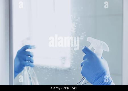 Vista ritagliata della donna governante mano in gomma blu guanti spruzzando liquido detergente chimico allo specchio mentre la pulizia bagno a casa. Casa Foto Stock
