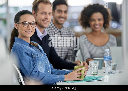 Riunione improvvisata per ottenere le idee migliori insieme. Gruppo di colleghi seduti a un tavolo sorridendo alla telecamera. Foto Stock