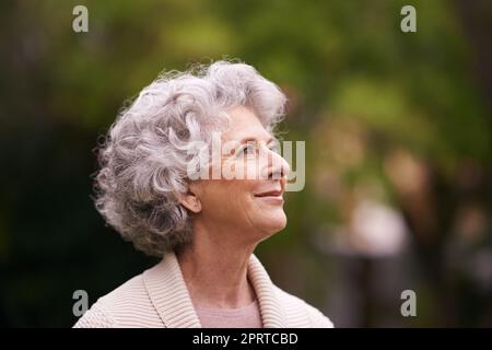 Perso in ricordi felici. Una donna anziana profonda nel pensiero mentre si trova fuori. Foto Stock