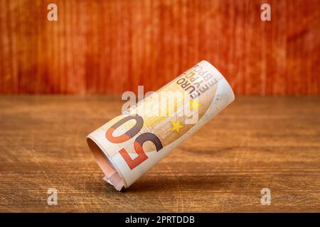 Rotolo di cinquanta banconote in euro che cadono su sfondo di legno Foto Stock