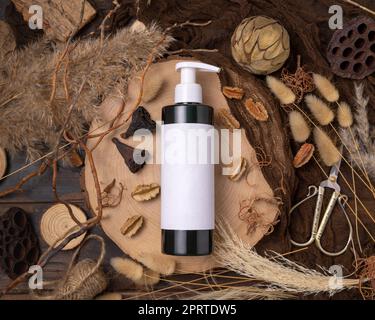 Una bottiglia cosmetica con pompa su legno vicino alle decorazioni boho naturali vista dall'alto. Etichetta Mockup Foto Stock