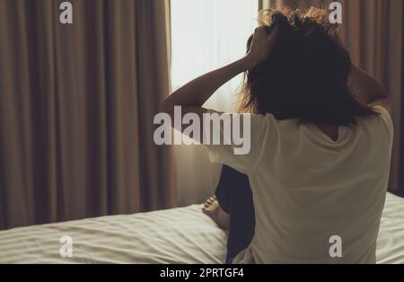 Concetto della giornata mondiale della salute mentale. Vista posteriore di una donna arrabbiata che mette la mano sulla testa e tira i capelli. Donna con malattia mentale seduta sul letto in camera da letto. Donna con problemi di salute mentale. Persona stressata e nervosa. Foto Stock