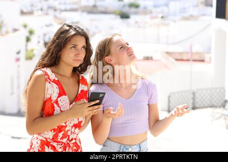 Turisti persi che controllano la posizione sullo smartphone in una strada bianca della città durante le vacanze estive Foto Stock