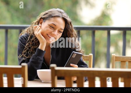 Donna in un balcone che sorride usando il telefono Foto Stock