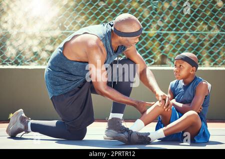 Pallacanestro ginocchio infortunio bambino con papà messo emergenza band aiuto per sport allenamento gioco incidente a campo da basket. Squadra africana di padre nero e bambino ferito con dolore alle gambe curativo e intonaco ferito Foto Stock