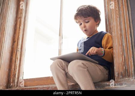 HES tech savvy già. Un ragazzino carino che usa un tablet mentre si siede su un davanzale. Foto Stock